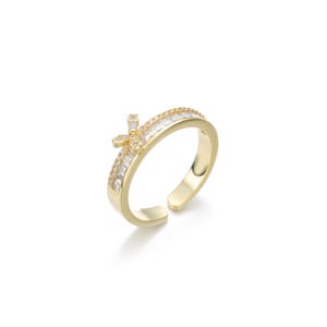 Puede incluir: Un anillo ajustable de oro con un diseño de flor de cristal transparente y una banda de cristales baguette transparentes.