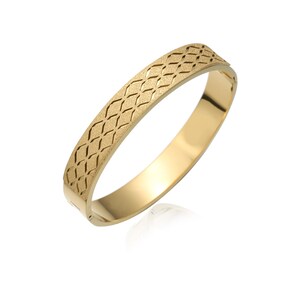 May include: A gold-colored bangle bracelet with a textured, diamond-patterned band. The bracelet has a smooth, polished interior and a clasp closure. The jewelry is displayed on a white background, highlighting its reflective surface.