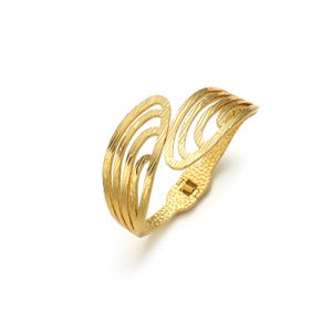 May include: A gold-toned hinged cuff bracelet featuring a series of curved, open-work bands with a textured finish. The design consists of multiple parallel lines that create a layered, wing-like appearance, secured by a small metal hinge mechanism.