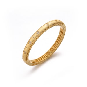 May include: A gold-toned hinged bangle bracelet with a matte, brushed finish. The outer surface features a repeating pattern of small, four-petaled floral motifs inlaid with tiny clear stones, accented by a delicate beaded edge along the sides.