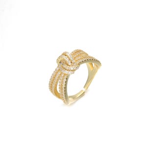 Puede incluir: Anillo de oro con diseño de nudo y piedras de circonita cúbica transparentes.