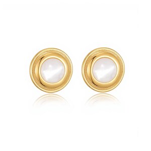 May include: A pair of gold-colored stud earrings with a round, white, mother-of-pearl center. The earrings have a textured, beaded border and a reflective surface.