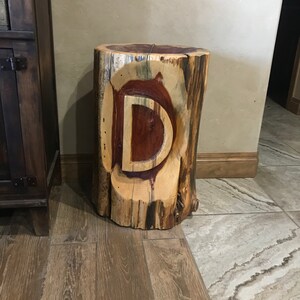 Peut inclure: Une table d'appoint en bois avec une lettre "D" sculptée sur le dessus. La table est faite d'un tronc d'arbre et a une finition en bois naturel.