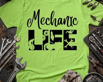 May include: A lime green t-shirt with the words "Mechanic LIFE" in black script and block letters. The word "LIFE" features mechanic-related graphics. Wrenches, gears, and other tools surround the shirt on a dark wooden surface.
