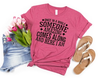May include: Pink t-shirt with black text that reads "Once in a while someone amazing comes along and here I am."