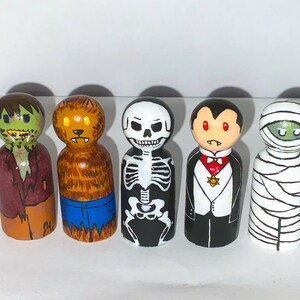Peut inclure: Cinq poupées en bois peintes pour ressembler à des monstres classiques d'Halloween. Les poupées sont peintes dans différentes couleurs, notamment le vert, le marron, le blanc, le noir et le rouge. Les monstres comprennent un zombie, un loup-garou, un squelette, un vampire et une momie.