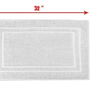 May include: A rectangular white bath mat with a textured surface and a double-bordered frame design. Red arrows and text indicate the dimensions of the mat as 32 inches in length and 22 inches in width, providing a clear visual measurement.