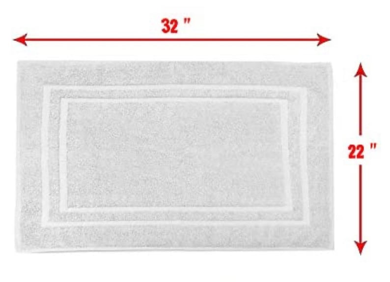 May include: A rectangular white bath mat with a textured surface and a double-bordered frame design. Red arrows and text indicate the dimensions of the mat as 32 inches in length and 22 inches in width, providing a clear visual measurement.