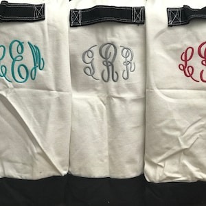 May include: Three white canvas laundry hampers with black handles and black bottoms. The hampers are monogrammed with the letters "LRJ" in different colors: teal, gray, and red.