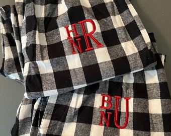 May include: Two pairs of black and white plaid pajama pants with red embroidered initials. The top pair has the initials "HNR" and the bottom pair has the initials "BNU".