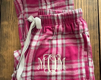 May include: Pink and white plaid pajama pants with a gray drawstring and the monogram "MOM" embroidered on the front.