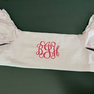 May include: A pink and white striped baby onesie with a white zipper and a pink monogrammed "BSH" on the front.