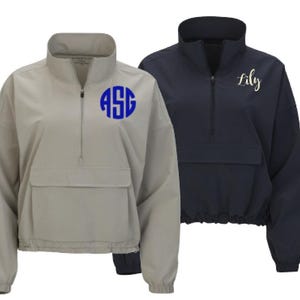 May include: Two quarter-zip pullovers. One is light gray with a blue monogram "ASG" on the chest. The other is navy blue with the name "Lily" in gold script. Both have a stand-up collar and a front pocket.