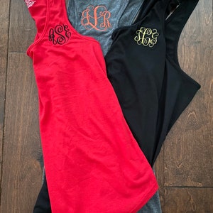 May include: Three tank tops with different colors and monograms. The tank tops are red, gray, and black. The monograms are in black, orange, and gold.