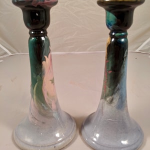 Puede incluir: Un par de candelabros de cerámica con un esmalte azul y blanco. Los candelabros están decorados con diseños florales pintados a mano en tonos de rosa, verde y amarillo.