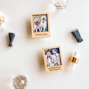 Könnte beinhalten: Zwei Holzbilderrahmen mit Fotos und graviertem Text. Der erste Rahmen zeigt ein Foto von zwei Hunden und den Text "i love you". Der zweite Rahmen zeigt ein Foto eines Paares und den Text "small moments big memories".