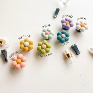 Pode incluir: Conjunto de aromatizadores de carro de flores de feltro em várias cores, incluindo lavanda, natural, agave, oceano, chartreuse, mostarda e goiaba. As flores estão presas a clipes e são etiquetadas com seus aromas correspondentes.