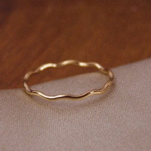 May include: A thin gold ring with a wavy, textured band.