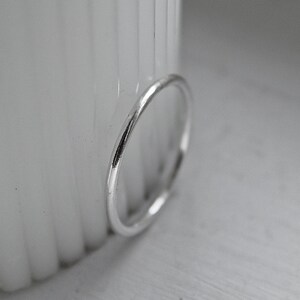 May include: A simple silver ring with a polished surface. The ring is positioned against a blurred white backdrop, accentuating its understated, elegant design. This piece of jewellery is suitable for everyday wear.