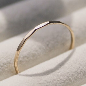 Könnte beinhalten: Ein goldener Ring mit einer strukturierten, facettierten Band sitzt in einer weißen Ringbox.