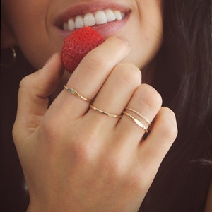 Close up of woman holding strawberry up to her face, whilst wearing dainty gold stacking rings