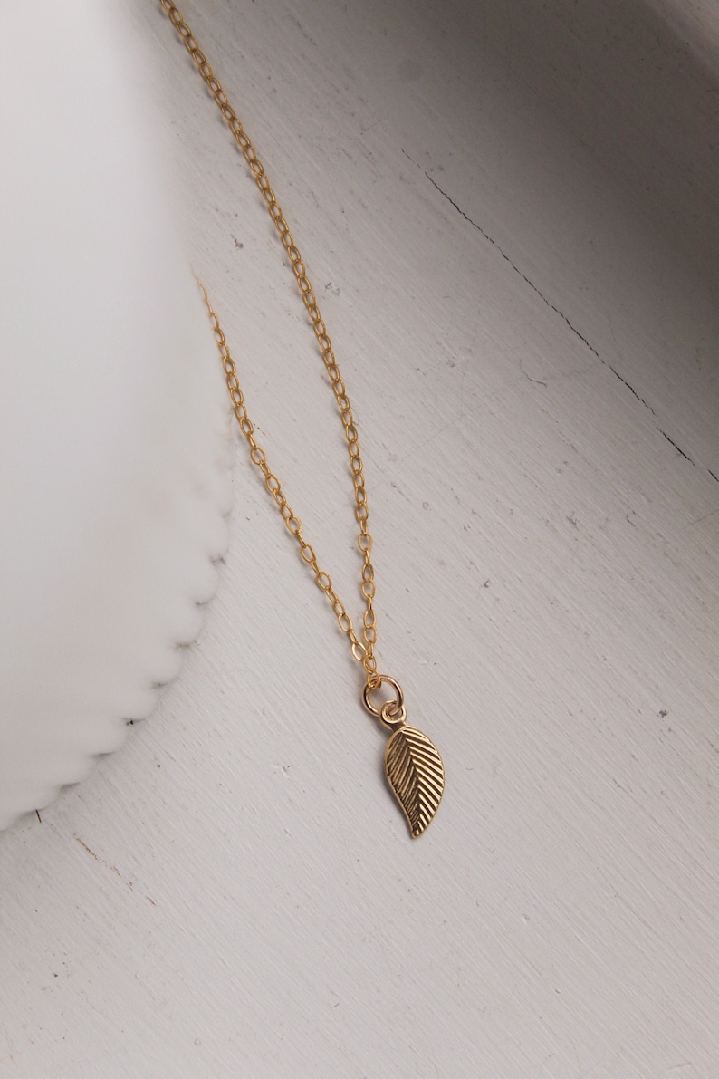 May include: A delicate gold chain necklace with a small, detailed leaf pendant.