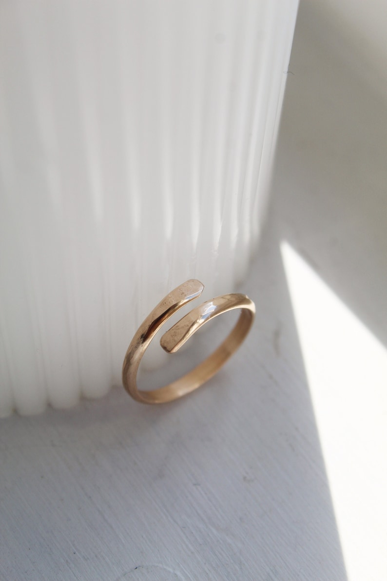 K&ouml;nnte beinhalten: Ein d&uuml;nner, offener Ring in Goldton mit einem schlichten, minimalistischen Design. Der Ring besteht aus einem einzigen Band, das sich um den Finger legt und sich dann auf sich selbst dreht.
