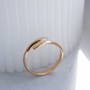 K&ouml;nnte beinhalten: Ein goldener Ring mit einem einzigartigen Design, mit einem gebogenen Band, das sich um den Finger legt.
