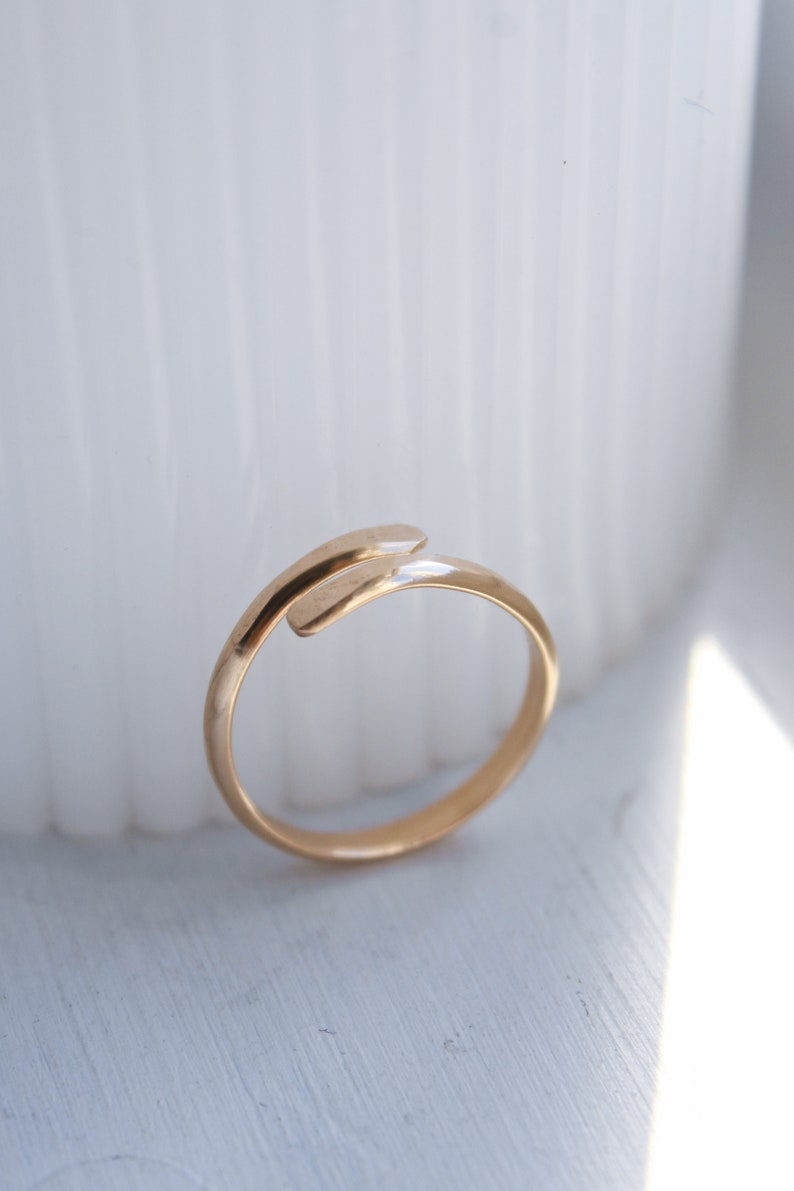 K&ouml;nnte beinhalten: Ein goldener Ring mit einem einzigartigen Design, mit einem gebogenen Band, das sich um den Finger legt.