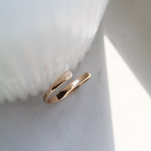K&ouml;nnte beinhalten: Ein einfacher goldener Ring mit einem gedrehten Design. Der Ring ist offen und kann an verschiedene Fingergr&ouml;&szlig;en angepasst werden.