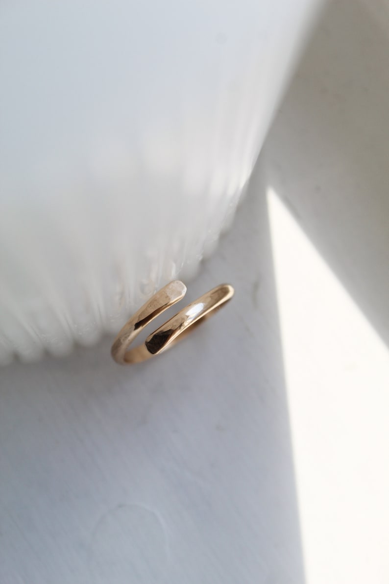 K&ouml;nnte beinhalten: Ein einfacher goldener Ring mit einem gedrehten Design. Der Ring ist offen und kann an verschiedene Fingergr&ouml;&szlig;en angepasst werden.