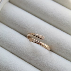 K&ouml;nnte beinhalten: Ein goldener, geh&auml;mmerter Ring mit einem einzigartigen, offenen Design. Der Ring wird in einer wei&szlig;en Ringbox pr&auml;sentiert.