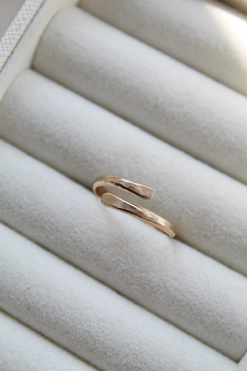 K&ouml;nnte beinhalten: Ein goldener, geh&auml;mmerter Ring mit einem einzigartigen, offenen Design. Der Ring wird in einer wei&szlig;en Ringbox pr&auml;sentiert.