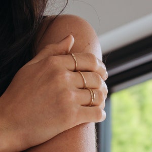 Close up of womans hand resting on arm, whilst wearing gold stacking rings