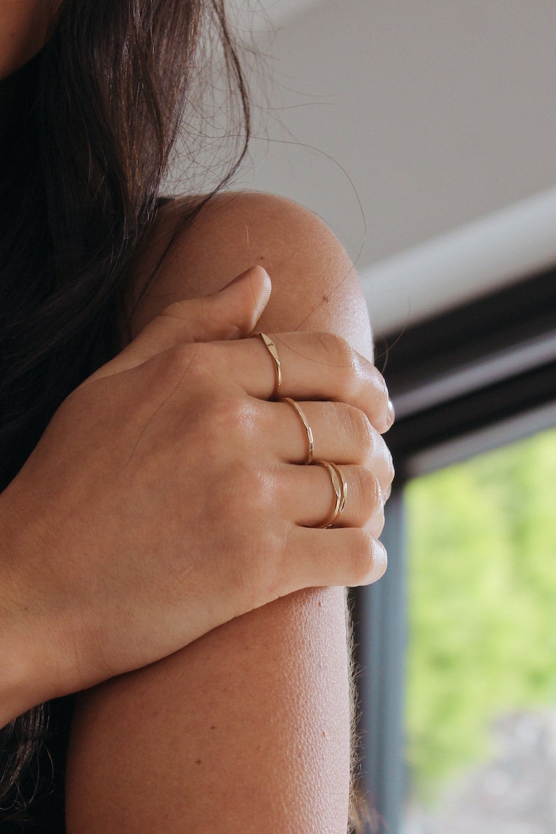 Close up of womans hand resting on arm, whilst wearing gold stacking rings