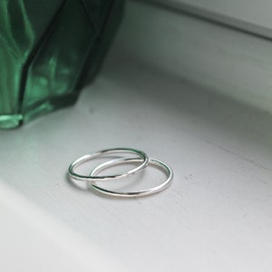Sterling Silver stackable rings stacked onto a white background with a green vase in the background. Silver rings on a window shelf.