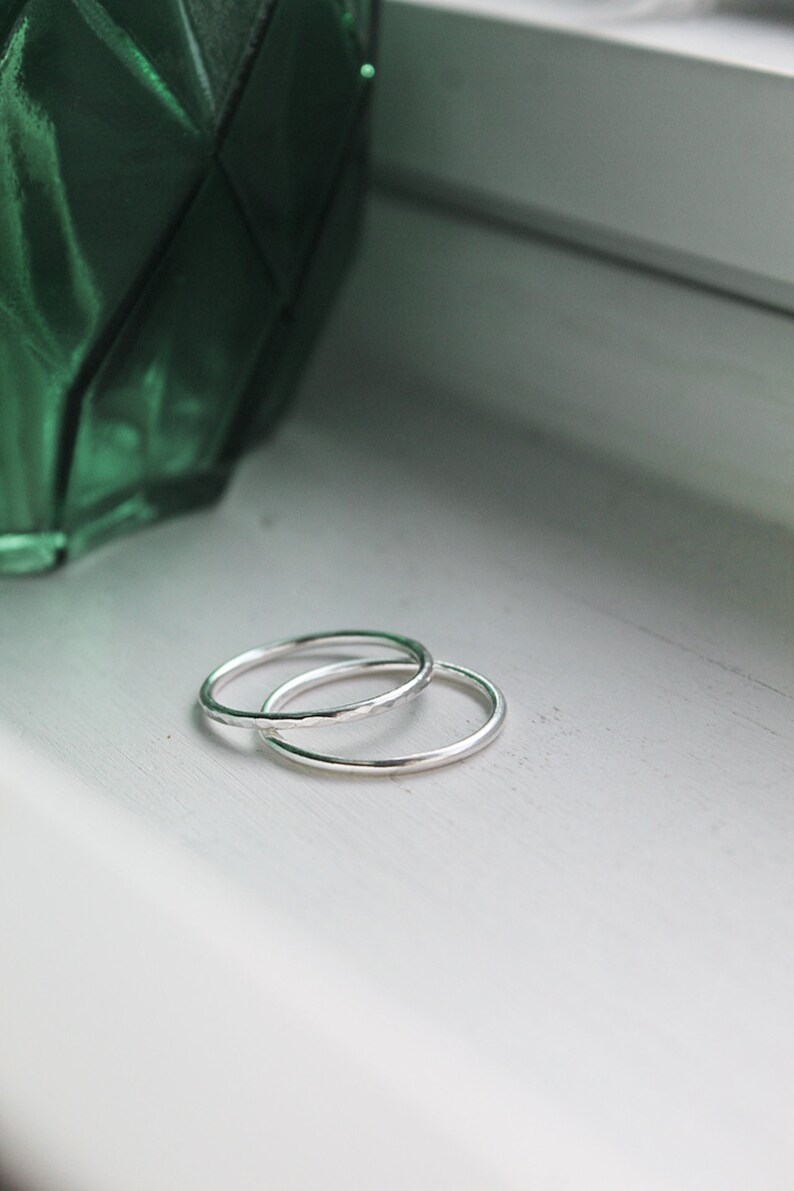 Sterling Silver stackable rings stacked onto a white background with a green vase in the background. Silver rings on a window shelf.