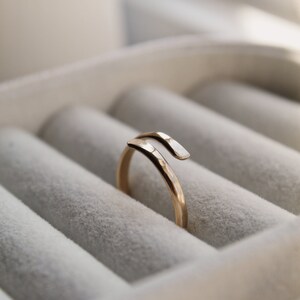 K&ouml;nnte beinhalten: Ein goldener Ring mit geh&auml;mmerter Oberfl&auml;che und einem einzigartigen, gedrehten Design. Der Ring wird in einer wei&szlig;en Ringbox pr&auml;sentiert.