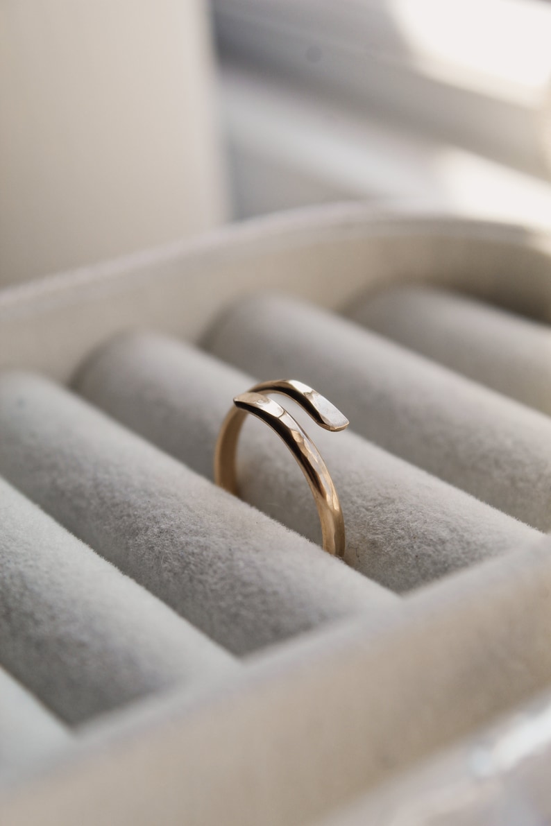 K&ouml;nnte beinhalten: Ein goldener Ring mit geh&auml;mmerter Oberfl&auml;che und einem einzigartigen, gedrehten Design. Der Ring wird in einer wei&szlig;en Ringbox pr&auml;sentiert.