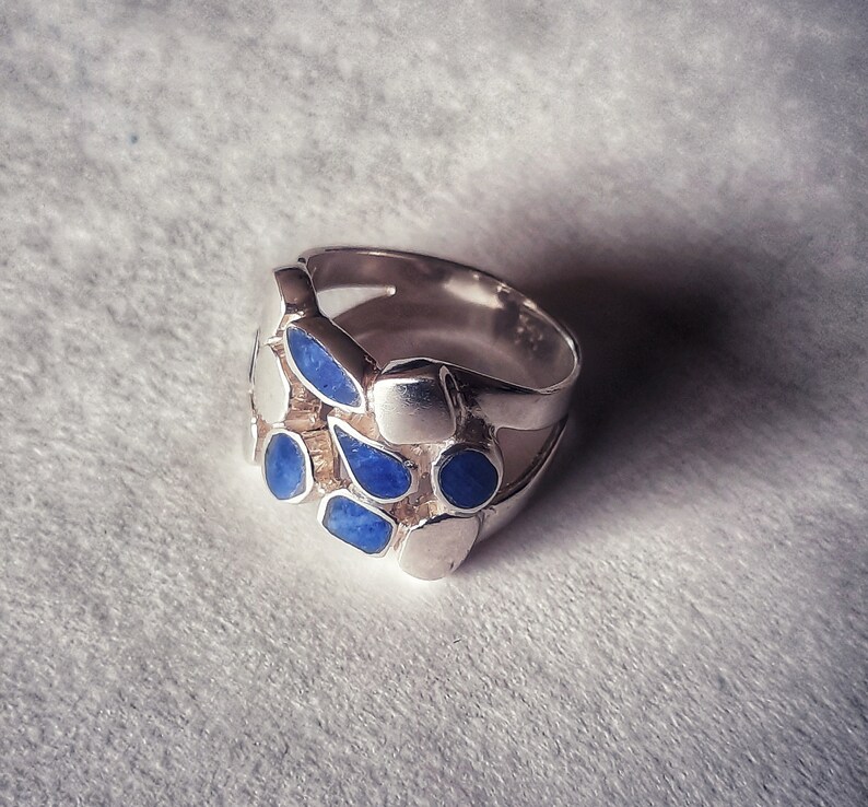 May include: A silver ring with a cluster of blue stones set in the band. The stones are irregularly shaped and have a slightly textured surface.