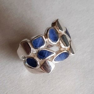 May include: A silver ring with a blue stone design. The ring is made of multiple small, irregular shapes that are set with blue stones.