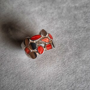 May include: A silver ring with a unique design featuring multiple red coral stones set in a silver band.