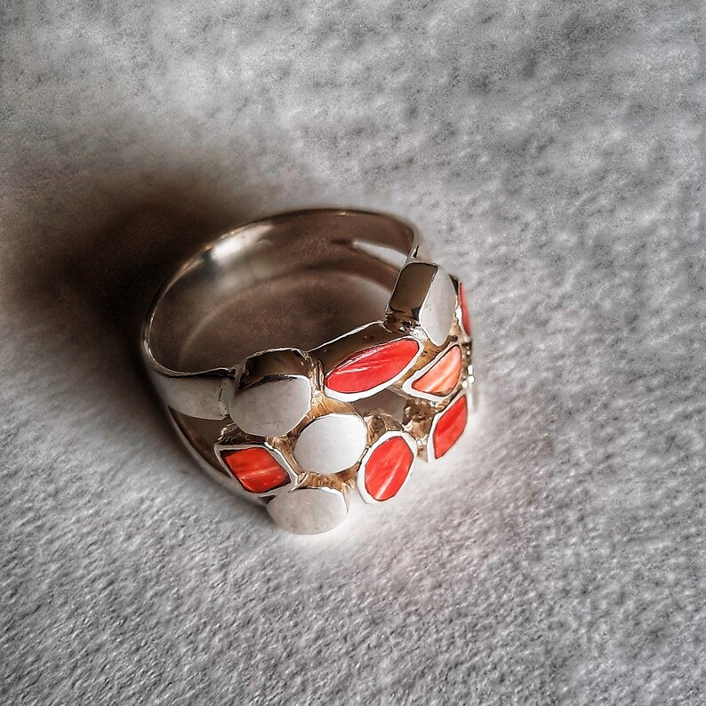May include: A silver ring with a unique design featuring a cluster of red and white stones. The stones are set in a silver band and create a geometric pattern.