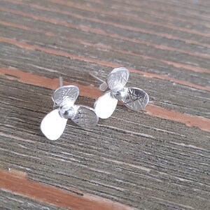 May include: A pair of silver propeller earrings. The propellers are textured and have a three-blade design.