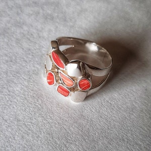 May include: A silver ring with a cluster of red and white stones set in the center. The ring has a double band design.