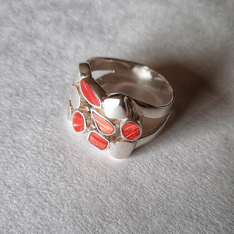 May include: A silver ring with a cluster of red and white stones set in the center. The ring has a double band design.