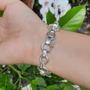 May include: A silver chain bracelet with a clasp closure. The bracelet is made of interlocking oval links.