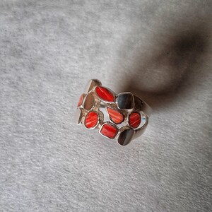 May include: A silver ring with a band of red coral stones set in a silver setting.