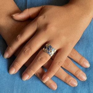 May include: A silver ring with a band of blue and white oval-shaped stones.