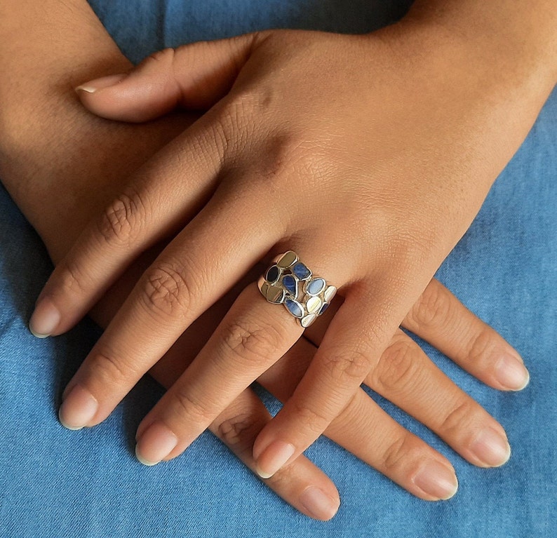 May include: A silver ring with a band of blue and white oval-shaped stones.